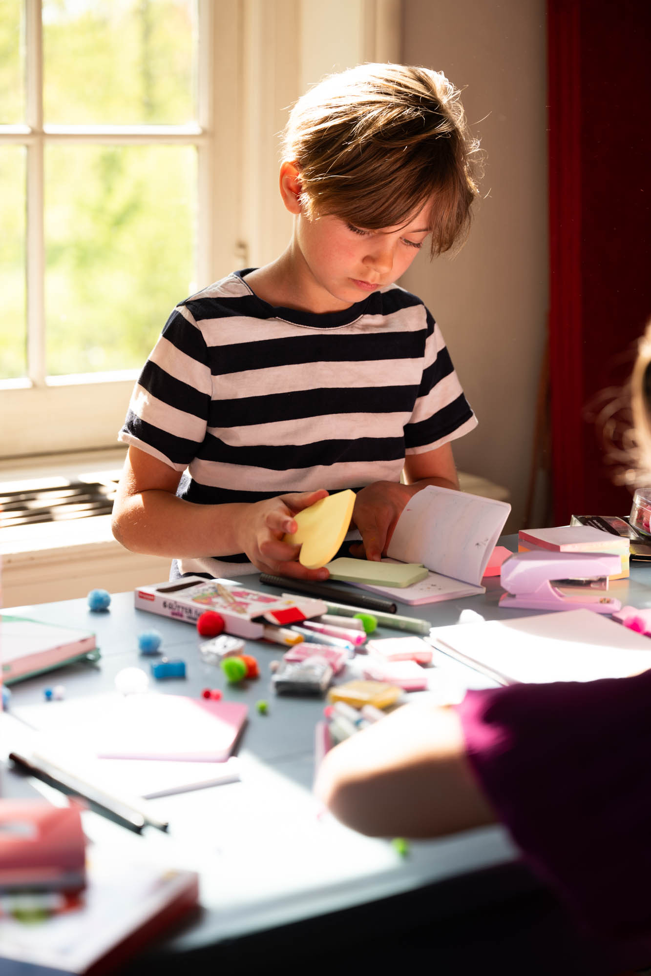 Jongen aan tafel met post-its en schoolspullen in tegenlicht
