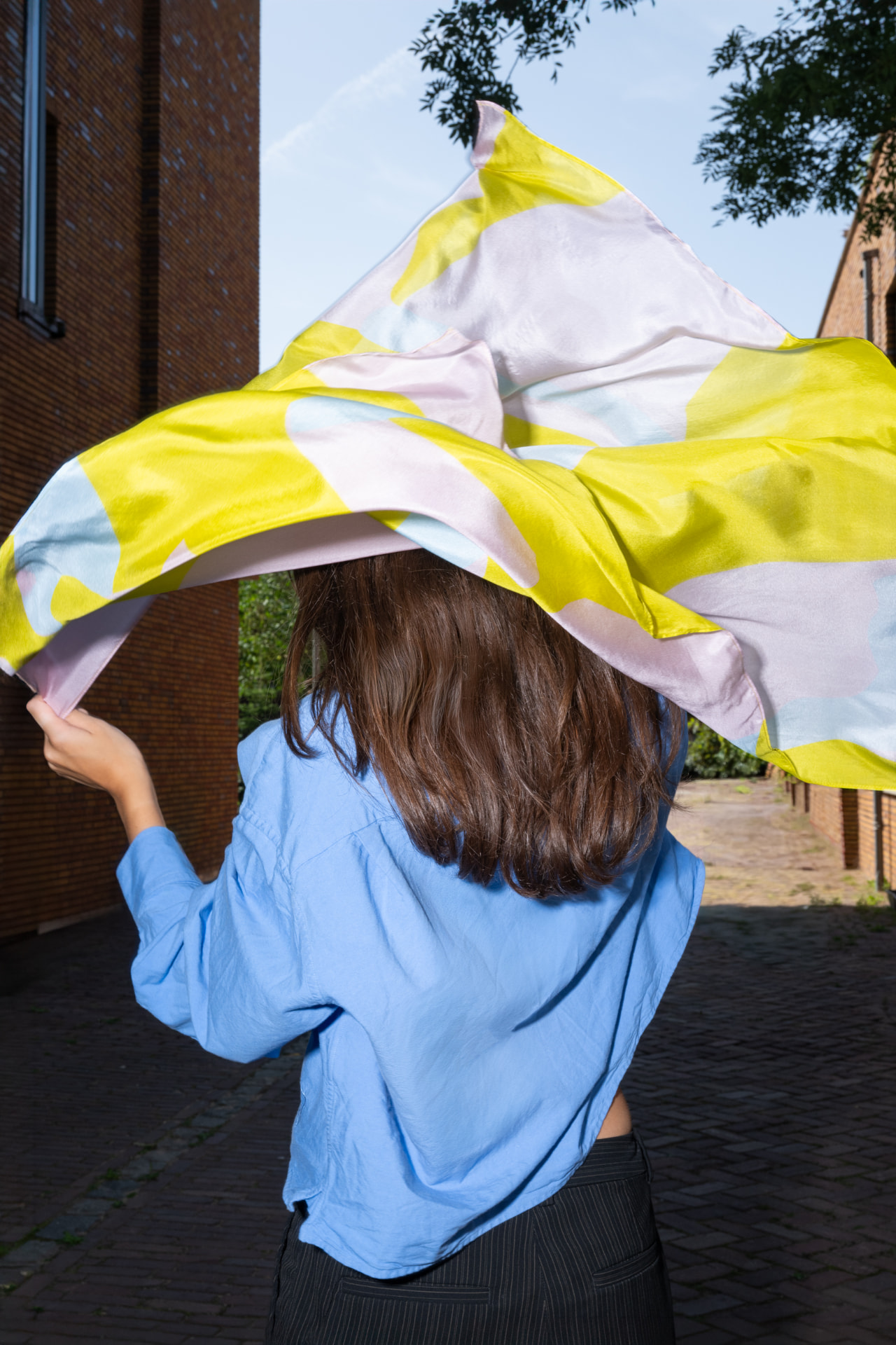 Vrouw houdt wapperende sjaal boven haar hoofd op straat