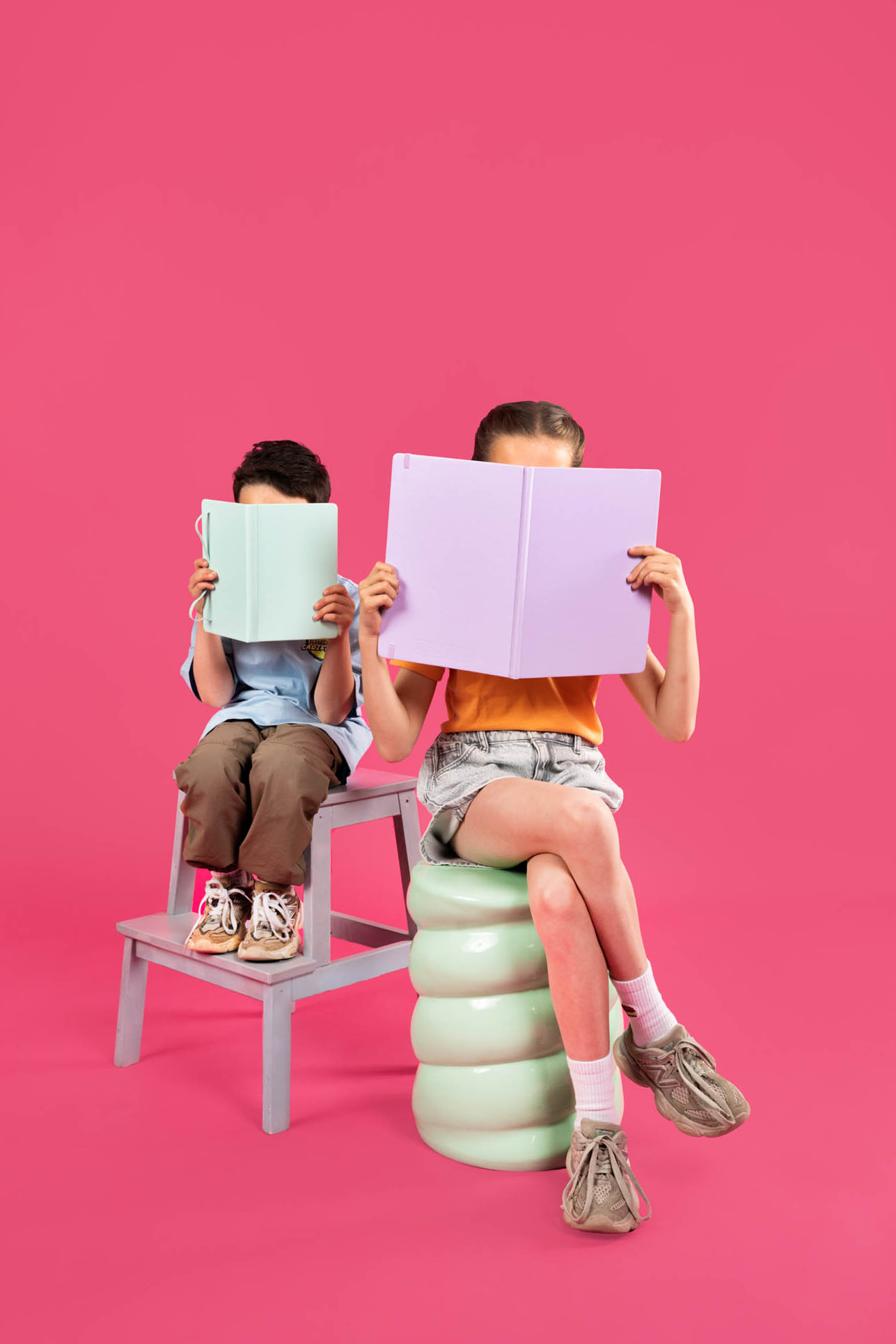 Twee kinderen met notitieboekjes voor hun gezicht op roze achtergrond